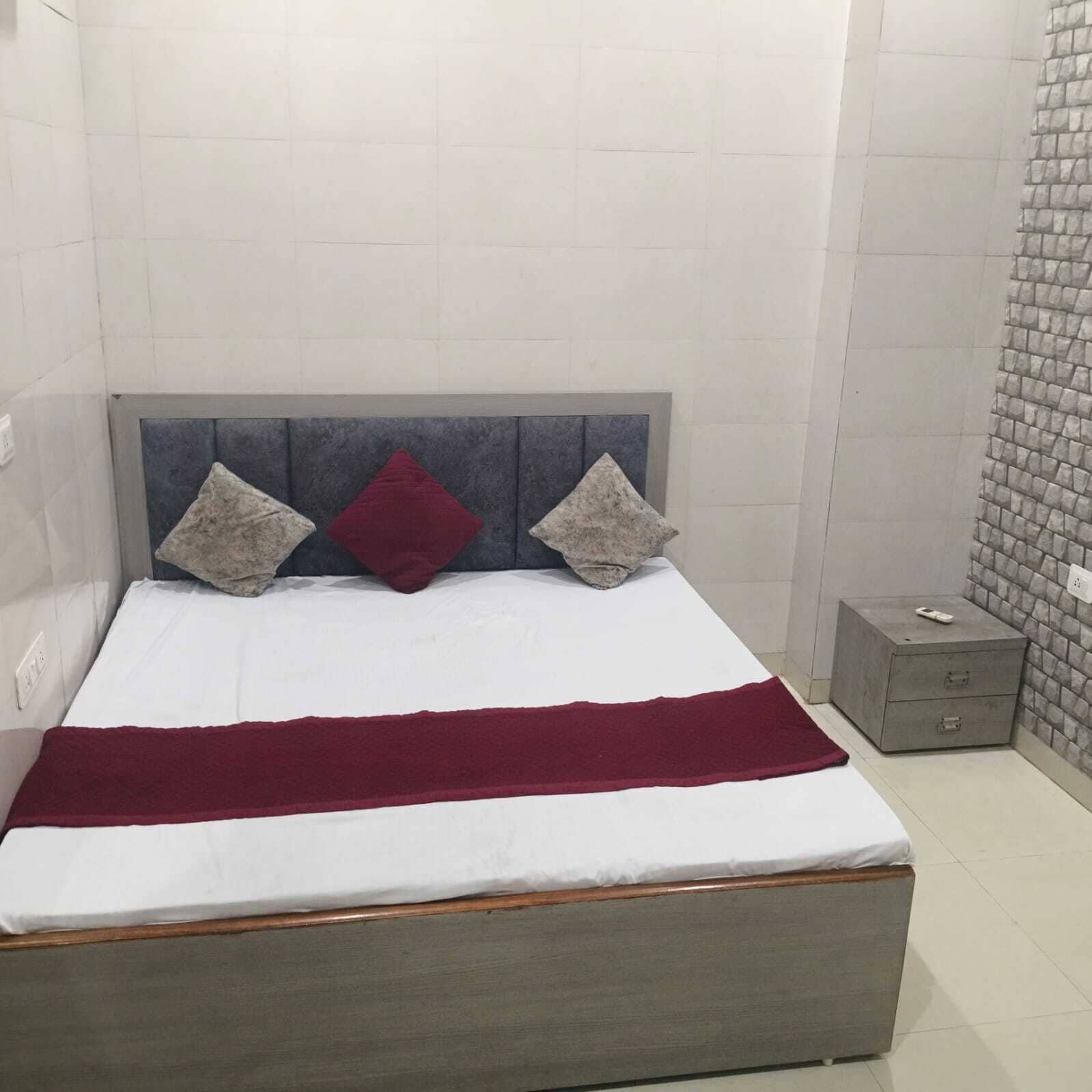 A bed with a grey headboard, white bedding, and two pillows, one red and two grey.