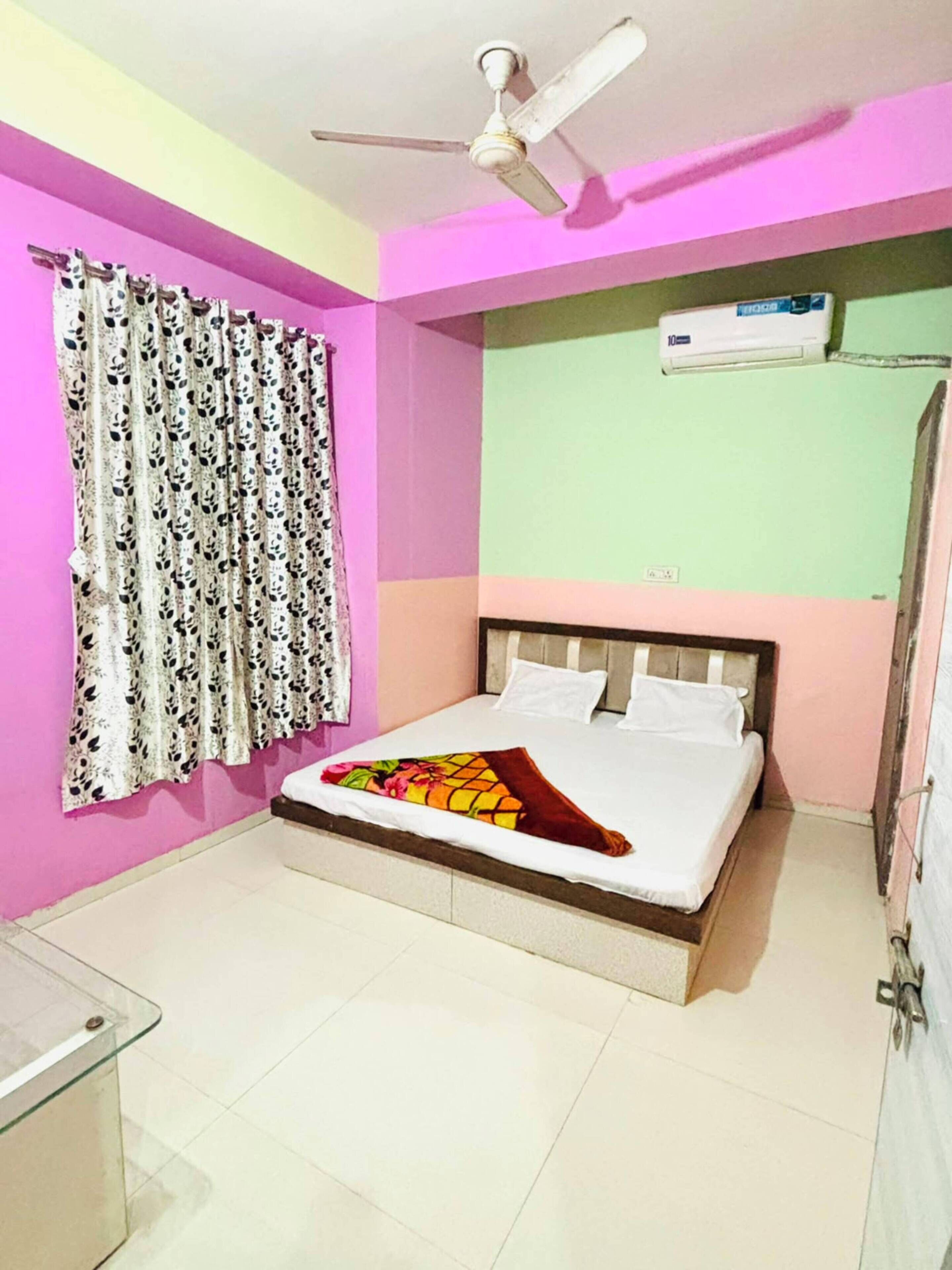 Un dormitorio con cama, ventilador de techo, ventana con cortinas estampadas y equipo de aire acondicionado.