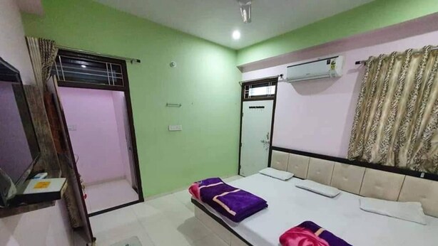 A hotel room with a bed, a window with curtains, an air conditioning unit, and a small table. - Hotel Arjun Palace (Shri Madhopur)