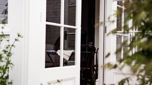 Une porte blanche avec une fenêtre, une chaise à l’intérieur et une plante à l’extérieur.