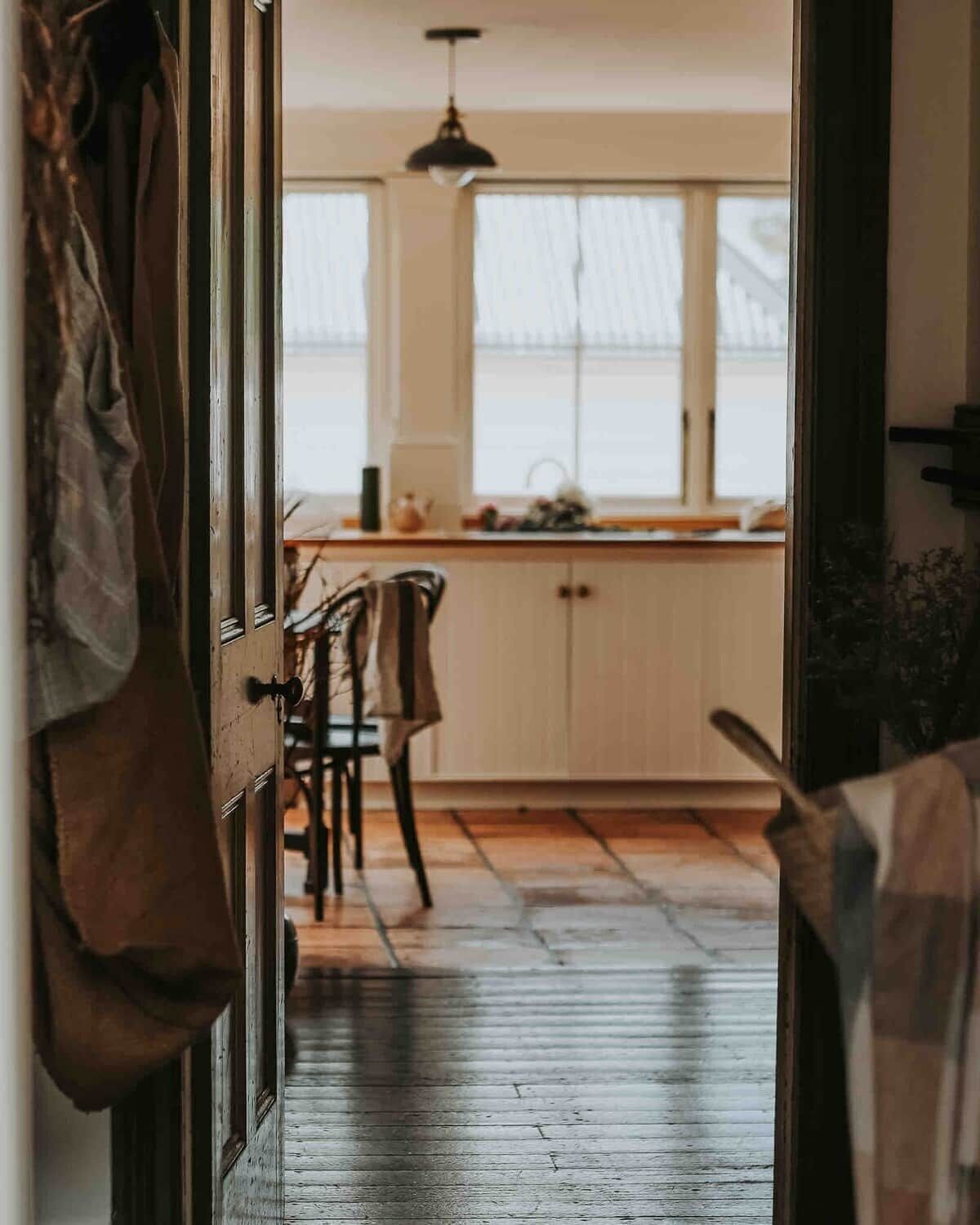 Una cocina con piso de madera, lámpara colgante y armarios.