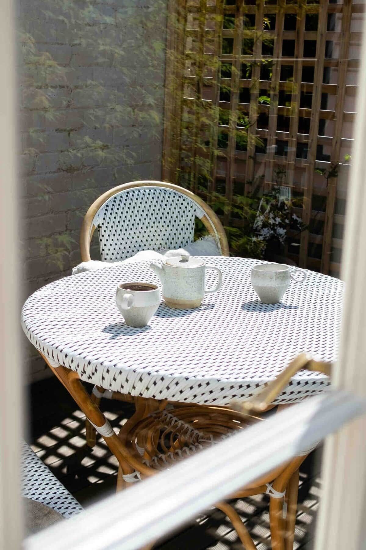 A round table with a white and black patterned tablecloth, two white ceramic cups, and a white ceramic teapot.
