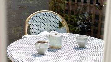 A round table with a white and black patterned tablecloth, two white ceramic cups, and a white ceramic teapot.