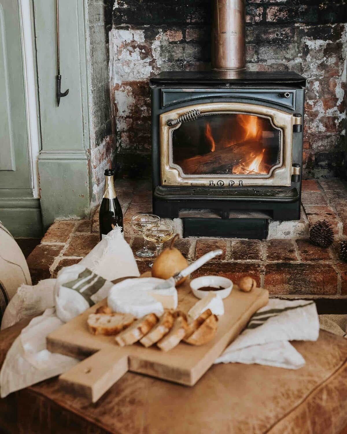 A wood-burning stove with a visible fire, a bottle, and a wooden cutting board with bread and a knife.