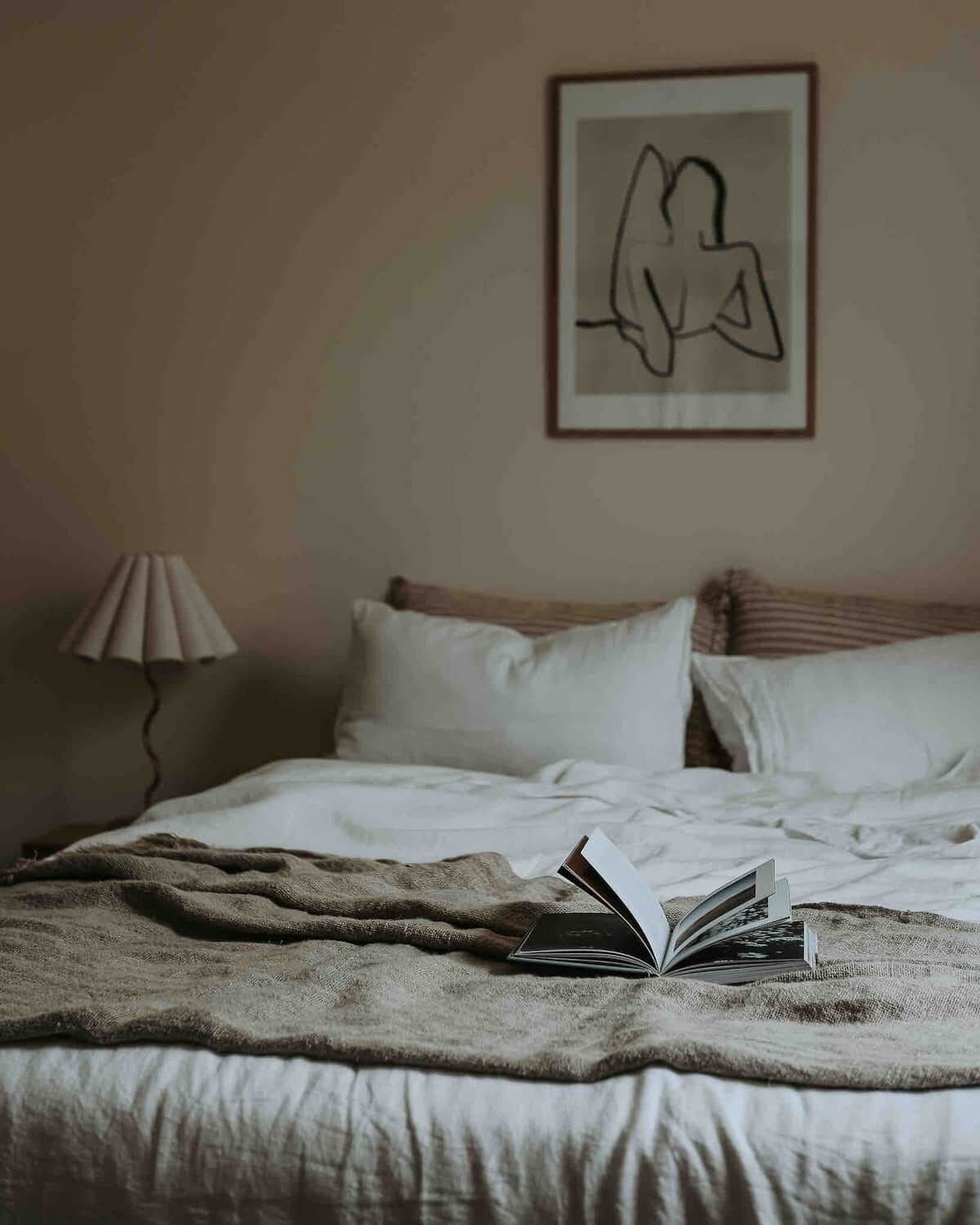 A bedroom with a bed, pillows, a blanket, a lamp, and a framed artwork on the wall.