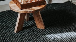 Um tabuleiro de xadrez sobre um banquinho de madeira numa sala de estar com lareira e sofá.