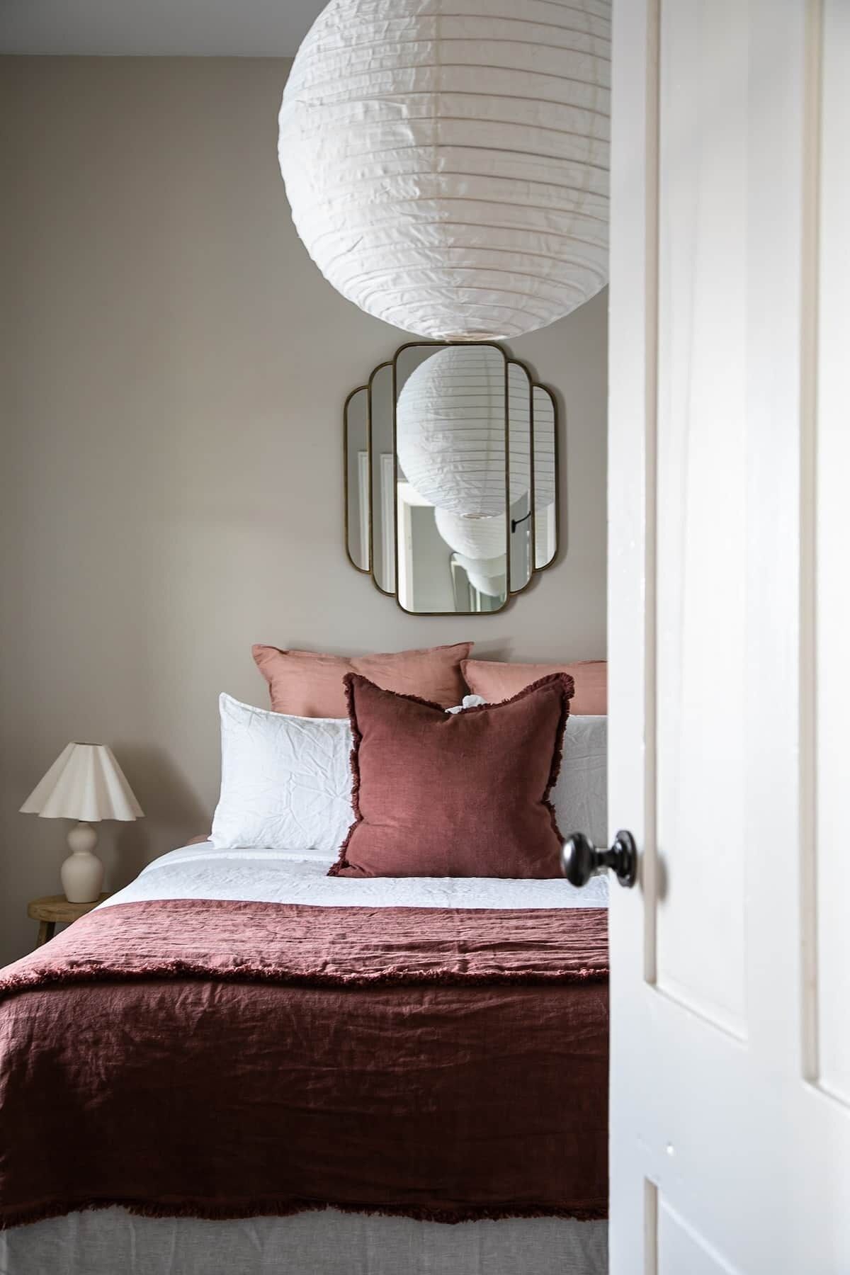 Quarto com cama, almofadas, abajur e luminária pendente.