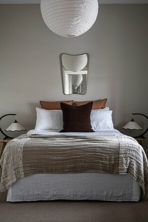 Ein Schlafzimmer mit einem großen Bett, zwei Nachttischlampen, einer Pendelleuchte und einem Spiegel an der Wand.