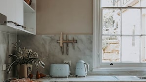 Uma cozinha moderna com armários brancos, fogão, lava-louças e uma janela com vista para um edifício.