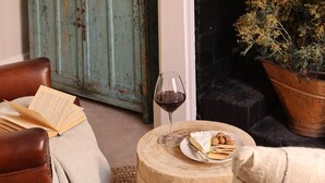 Uma sala de estar acolhedora com lareira, um aparador de madeira, uma poltrona de couro, uma mesa de madeira redonda com petiscos e um copo de vinho tinto.