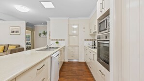 A compact kitchen with white cabinetry, a built-in oven, and a microwave. - 5 Zircon Street - Rainbow Beach (Rainbow Beach)