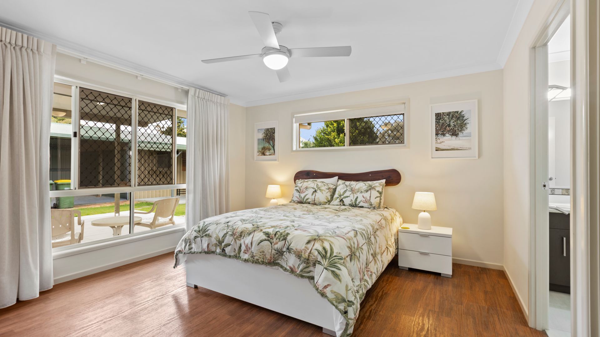 A bedroom with a bed, two bedside tables, a ceiling fan, and a window with a view of the outdoors.