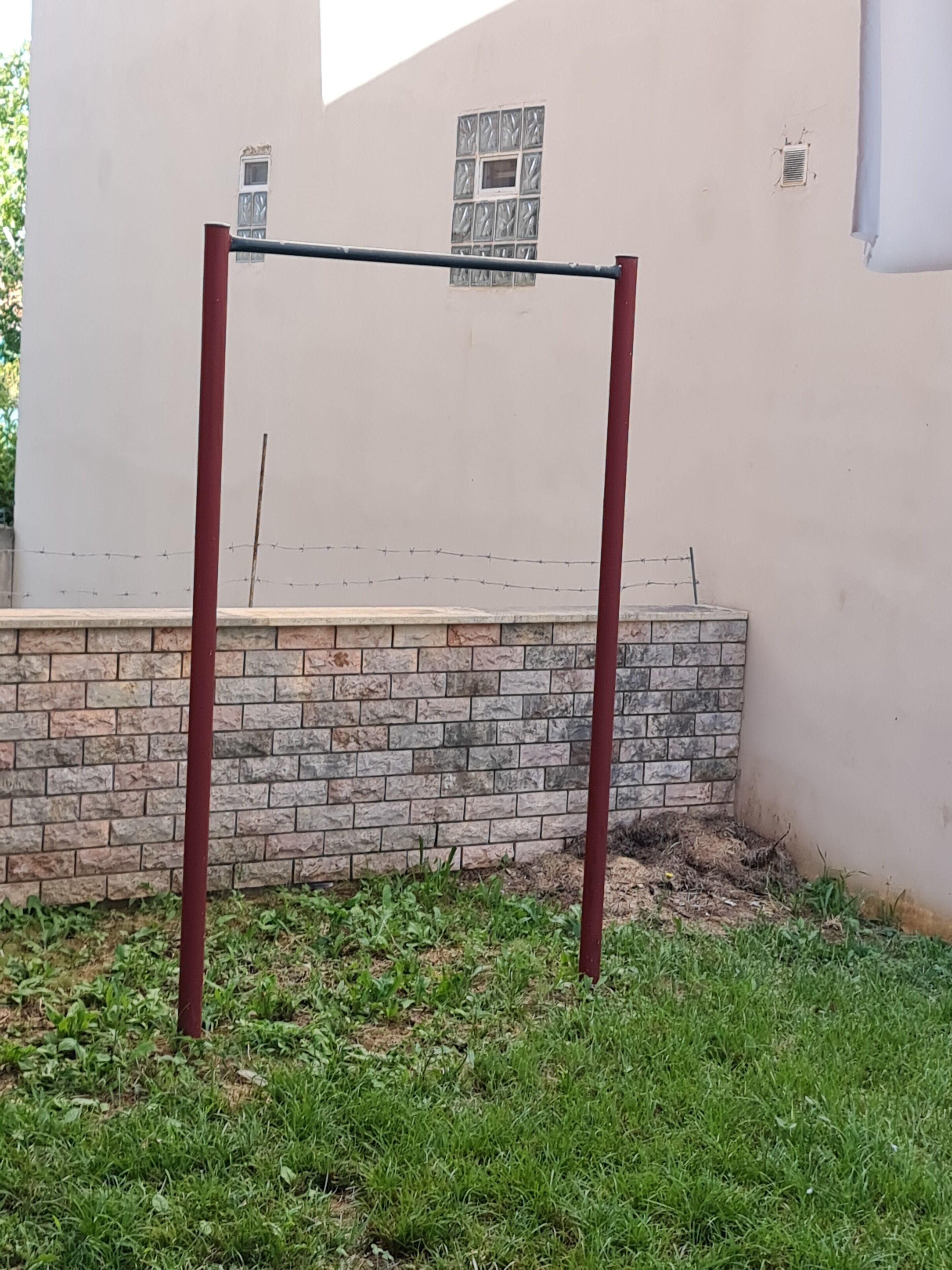 A metal bar structure in a grassy area with a stone wall and a building in the background.