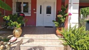 A red building with a white door, a window with bars, and potted plants.