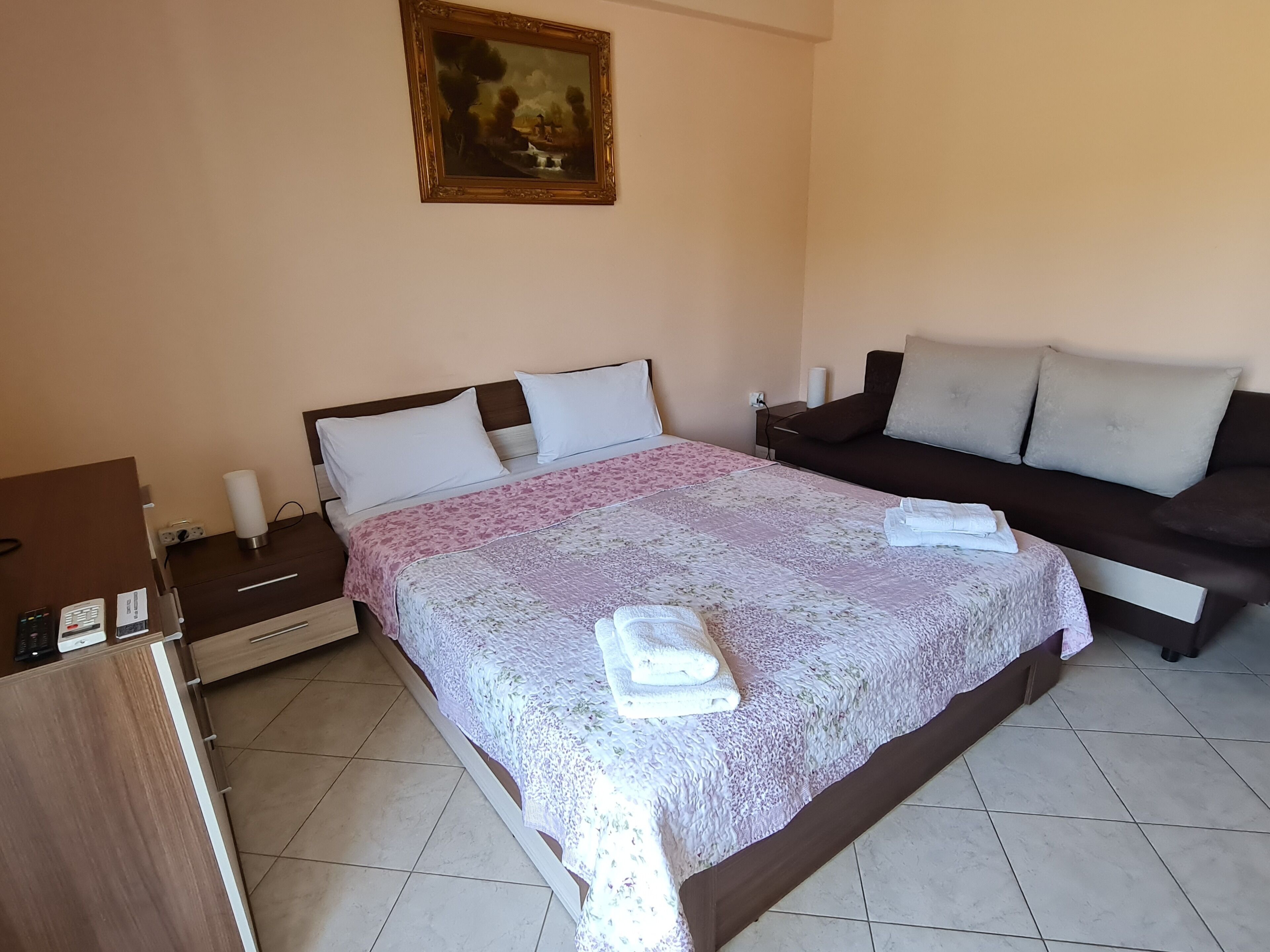A bedroom with a bed, bedside tables, a nightstand, a sofa, and a painting on the wall.