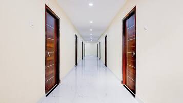 Un couloir bordé de portes en bois de chaque côté, avec un sol carrelé de carreaux blancs et des spots encastrés au plafond.