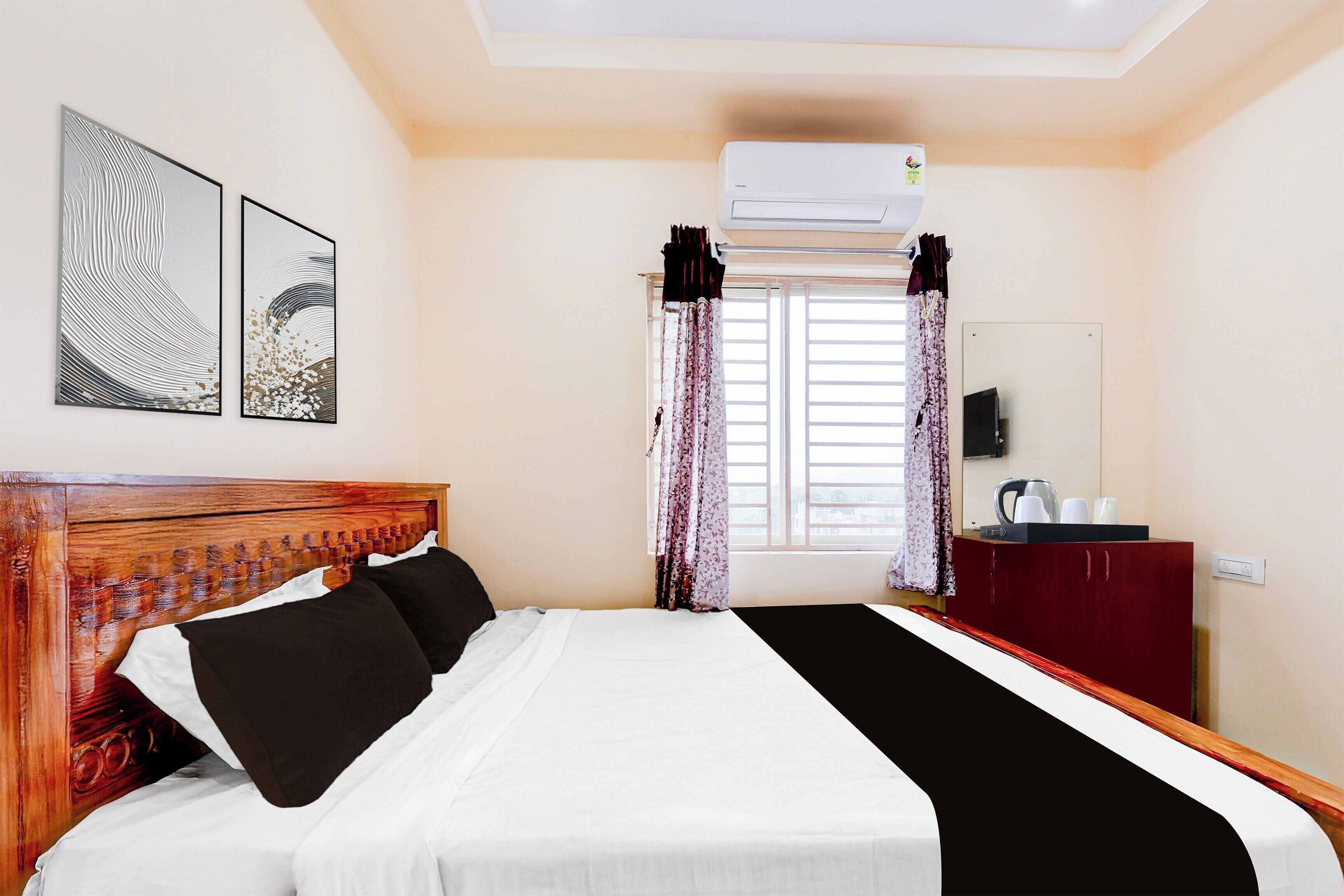 A hotel room with a bed, a wooden headboard, a flat-screen TV, a desk with a chair, and a window with curtains.