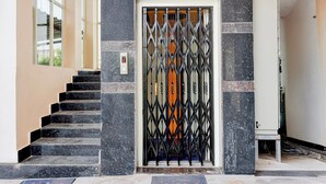 Une entrée d’immeuble avec un portail métallique, un escalier et un panneau de commande d’ascenseur fixé au mur.