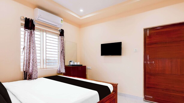 Une chambre à coucher avec un lit, un téléviseur fixé au mur, une armoire et une fenêtre avec des rideaux.