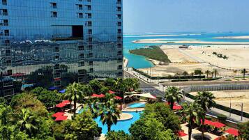 A high-rise hotel with a reflective glass facade, a pool area with palm trees, and a view of the beach and ocean.