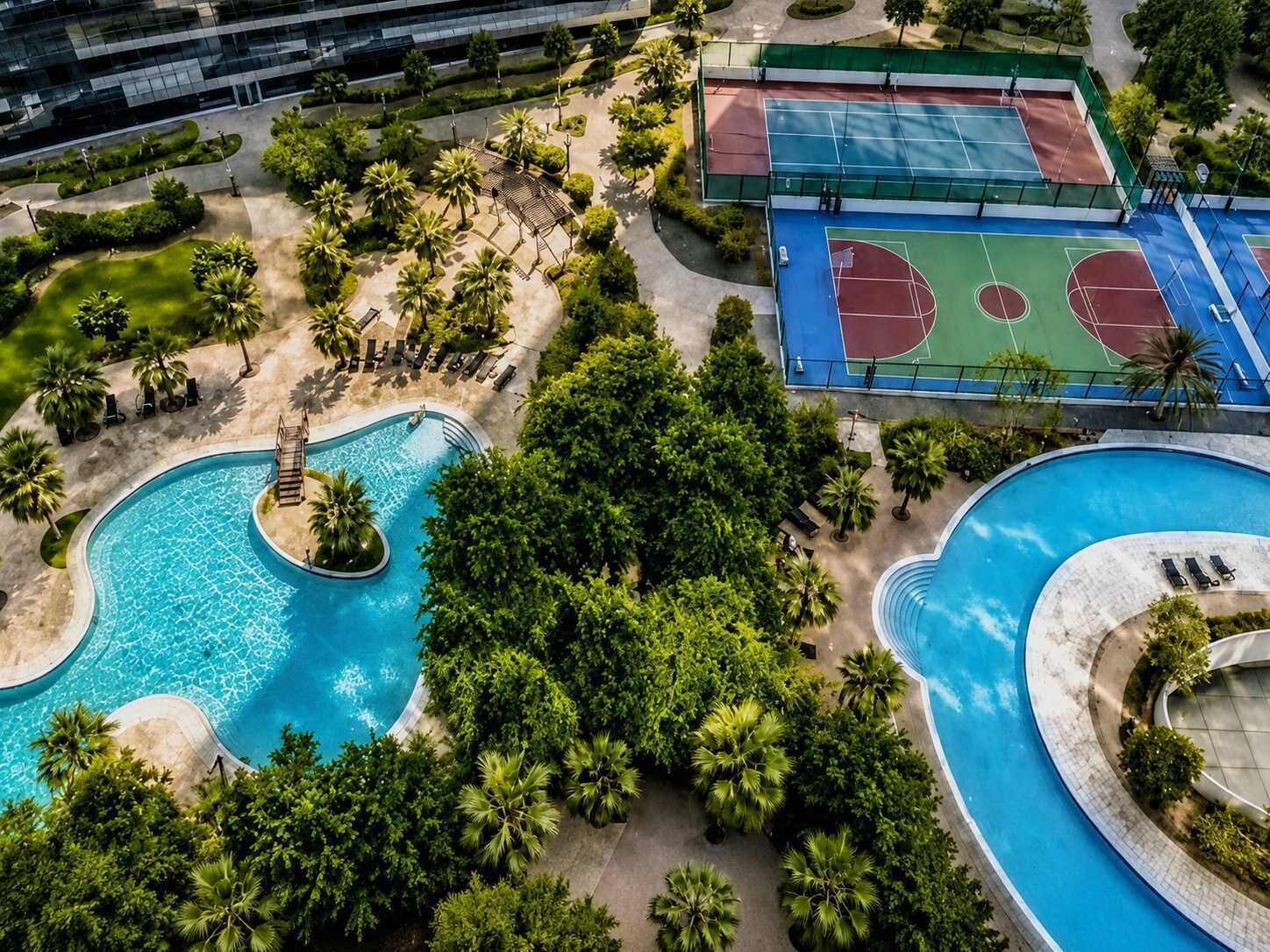 A large outdoor swimming pool with a central island, surrounded by lush greenery and palm trees.