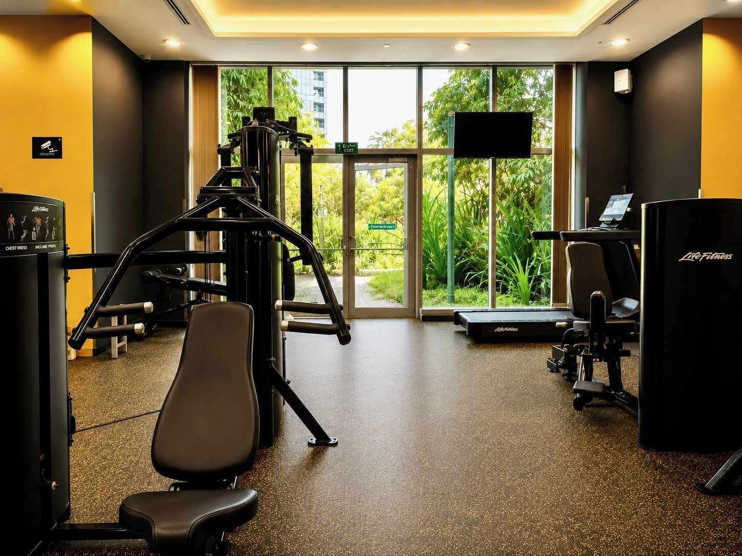 A gym with exercise equipment, a treadmill, and a large window with a view of greenery.