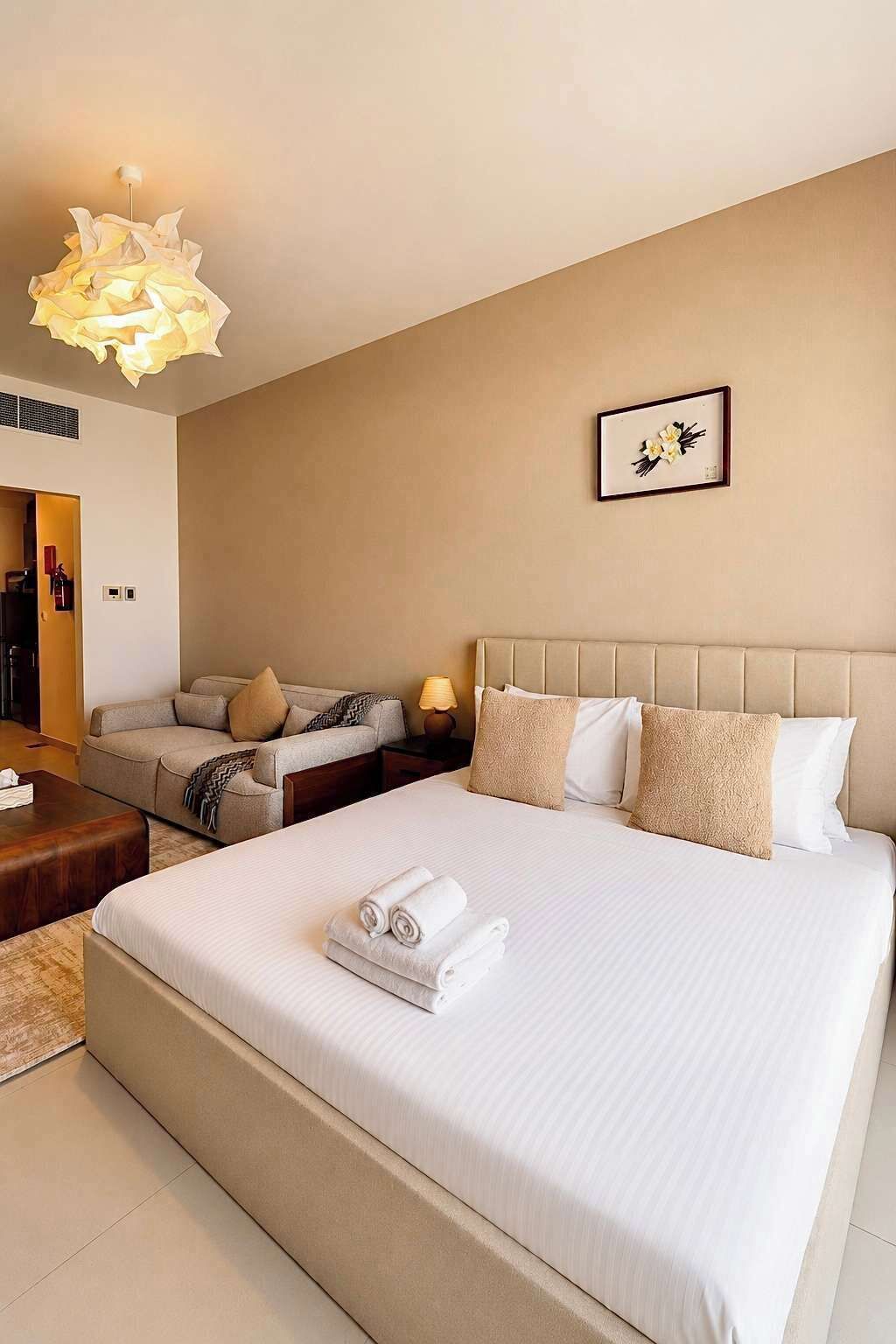A hotel room with a large bed, a bedside table with a lamp, a sofa, and a framed picture on the wall.