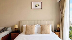 Ein Hotelzimmer mit einem großen Bett, zwei Nachttischen, einem Fenster mit Vorhängen und einem gerahmten Bild an der Wand.