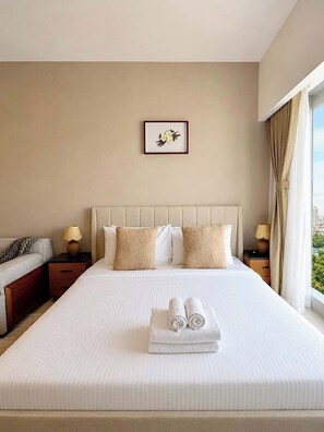 Ein Hotelzimmer mit einem großen Bett, zwei Nachttischen, einem Fenster mit Vorhängen und einem gerahmten Bild an der Wand.