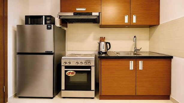 Eine kompakte Küche mit einem Edelstahl-Kühlschrank, einem Einbauofen, einem Herd und Holzschränken.