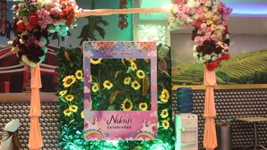 Un espacio decorado para un evento, con un arco floral, una foto enmarcada y un letrero que dice 'Nikah Celebration'.
