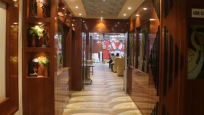 Pasillo de hotel con paneles de madera, suelo de mármol y una recepción con fondo rojo y cortinas blancas.