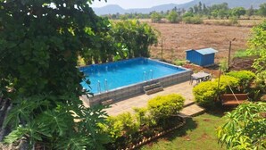 A rectangular swimming pool with steps leading into it, surrounded by a wooden deck and various plants. - Lonavala Farm stay (Mawal)