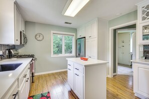 Eine Küche mit weißen Schränken, einem Edelstahlkühlschrank, einem Gasherd und einem Fenster mit Blick auf Bäume.