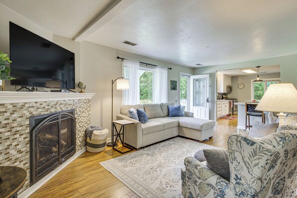 A living room with a fireplace, a sectional sofa, a television, and a kitchen in the background. - Updated Home Minutes to Downtown and Beach! (Sister Bay)