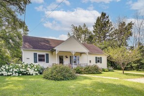 A single-story house with a porch, surrounded by a well-maintained lawn and various shrubs. - Updated Home Minutes to Downtown and Beach! (Sister Bay)