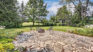 A stone patio with a fire pit, surrounded by a grassy area and trees. - Updated Home Minutes to Downtown and Beach! (Sister Bay)