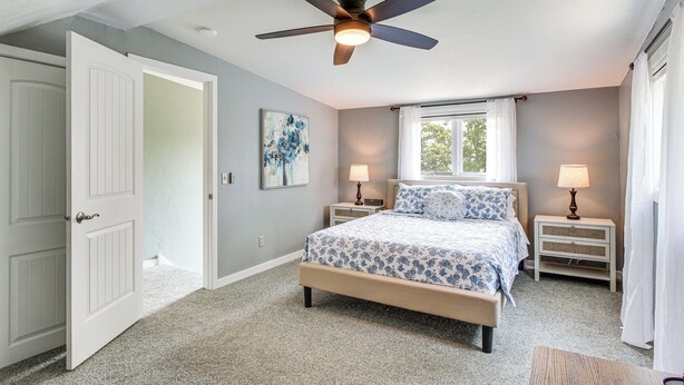 A bedroom with a bed, two bedside tables, a ceiling fan, a window with curtains, and a door. - Updated Home Minutes to Downtown and Beach! (Sister Bay)