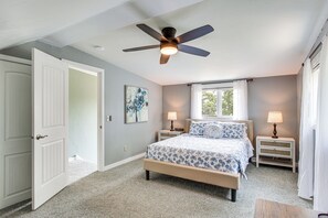 A bedroom with a bed, two bedside tables, a ceiling fan, a window with curtains, and a door. - Updated Home Minutes to Downtown and Beach! (Sister Bay)