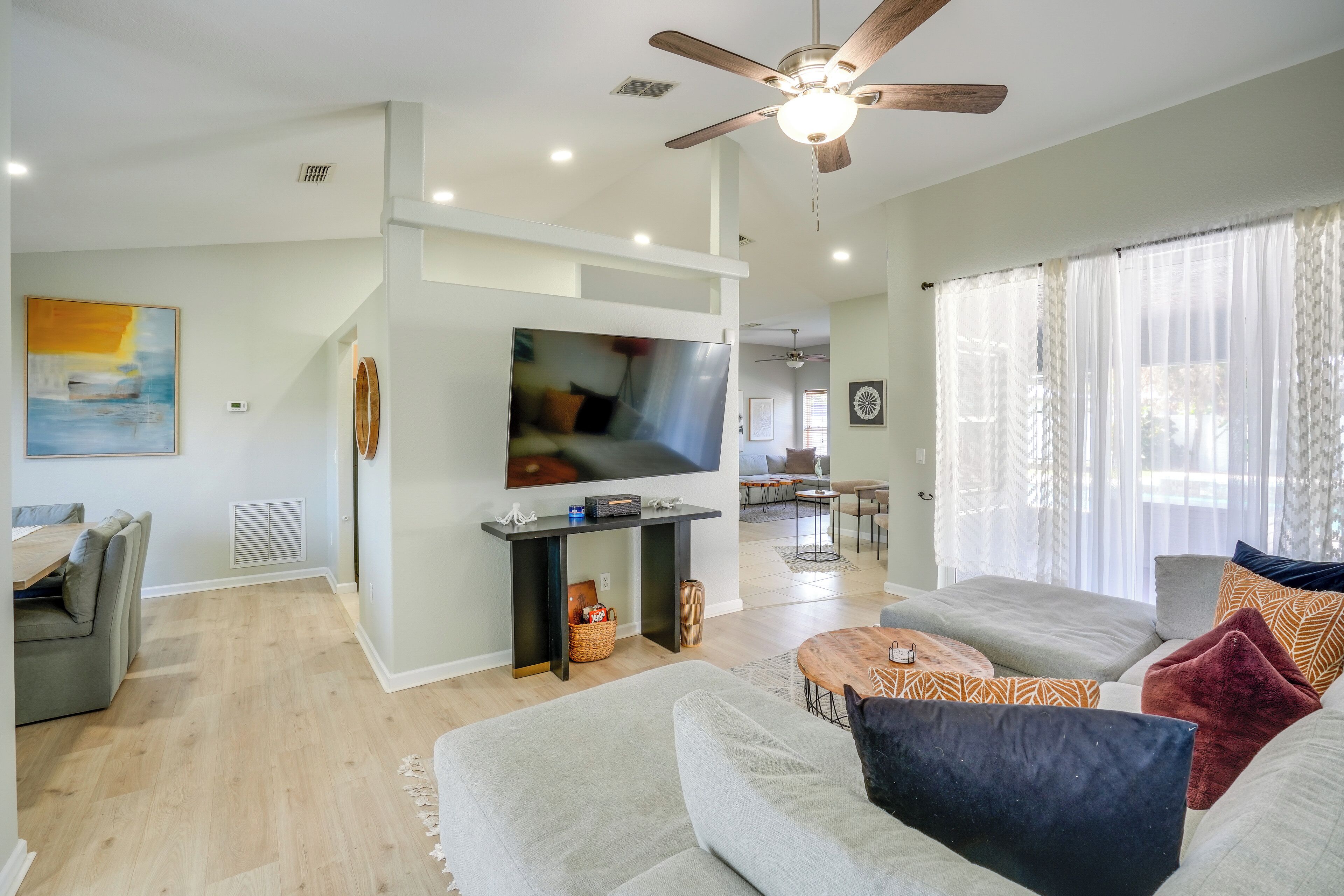 A modern living room with a ceiling fan, a flat-screen TV, and a dining area with a table and chairs.