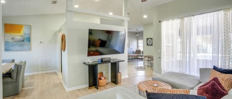Un salon moderne doté d’un ventilateur de plafond, d’un téléviseur à écran plat et d’un coin repas avec une table et des chaises.