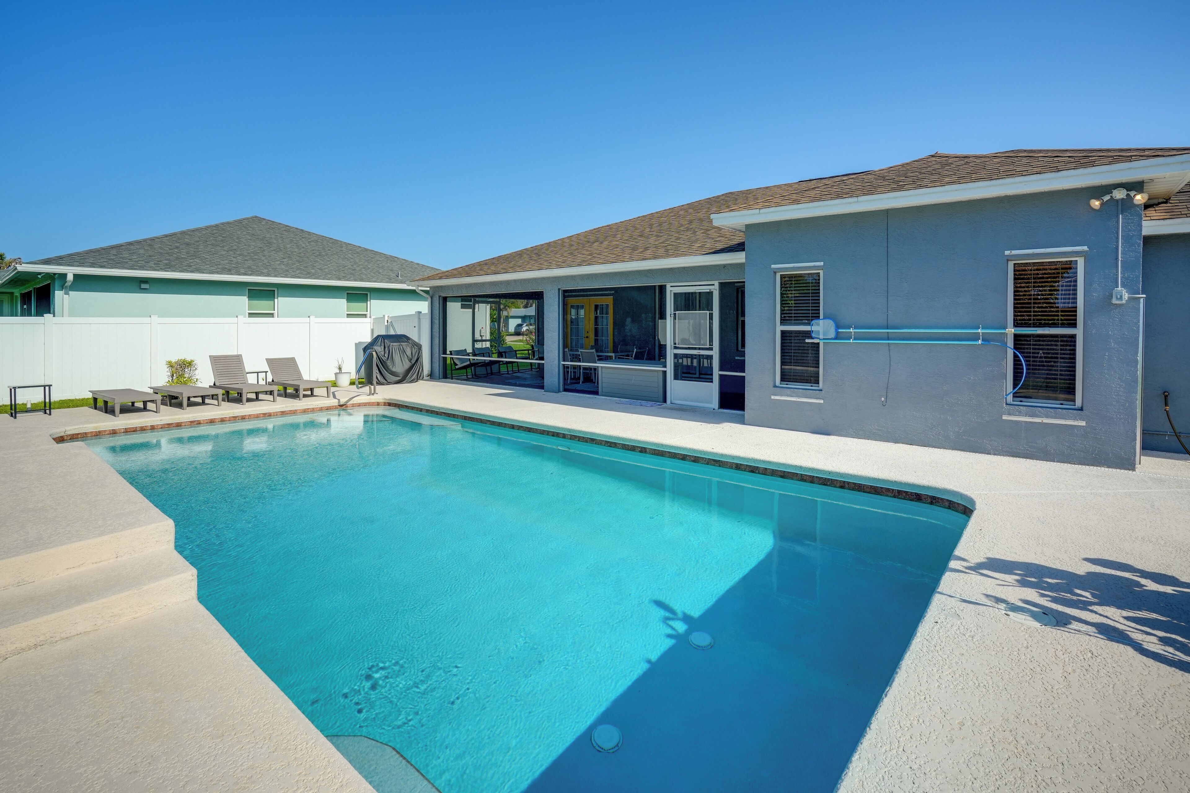 Une piscine avec un patio couvert, une cour arrière clôturée et une maison avec un toit en tuiles.