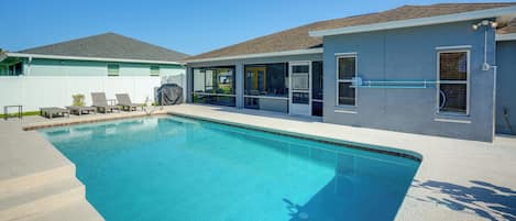 Une piscine avec un patio couvert, une cour arrière clôturée et une maison avec un toit en tuiles.