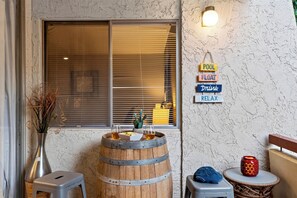 Une pièce comprenant un tonneau en bois, un petit tabouret, un cactus et un panneau mural sur lequel on peut lire les mots « PISCINE », « FLOTTER », « BOISSON » et « DÉTENTE ».