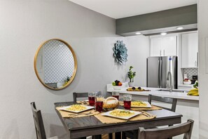 Une cuisine moderne avec des meubles blancs, un réfrigérateur en acier inoxydable et une table à manger dressée avec des assiettes remplies de nourriture et des boissons.