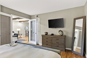 Ein Schlafzimmer mit Bett, Kommode, Fernseher und einer Tür zu einem anderen Raum.
