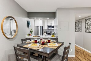 A modern kitchen with white cabinets, stainless steel appliances, and a dining area with a wooden table and chairs. - Resort Pool + Spa + Balcony | Fashion Square + Echo Canyon | Camelback Cabana (Scottsdale)