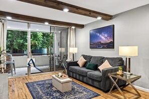 A modern living room with a grey sofa, a coffee table, and a glass coffee table with a lamp. - Resort Pool + Spa + Balcony | Fashion Square + Echo Canyon | Camelback Cabana (Scottsdale)