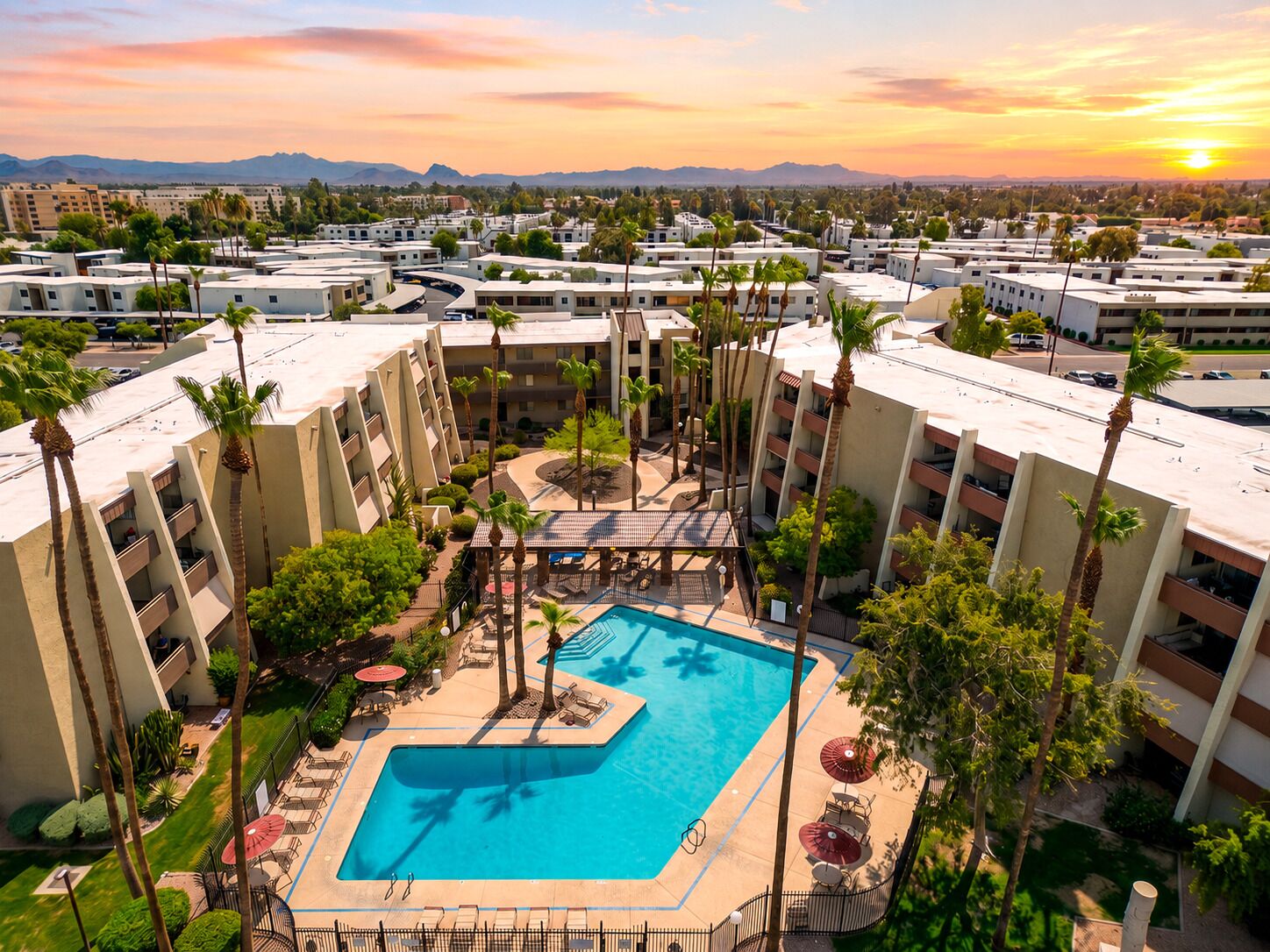 A hotel with a central swimming pool surrounded by palm trees and outdoor seating.