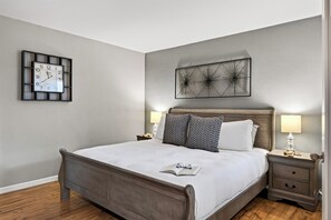 A neatly arranged bedroom with a bed, bedside lamps, a wall clock, and a decorative piece above the bed. - Resort Pool + Spa + Balcony | Fashion Square + Echo Canyon | Camelback Cabana (Scottsdale)